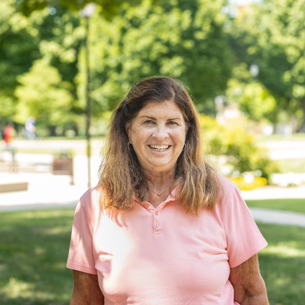 Lady with shoulder length dark hair wearing peach polo shirt standing outside